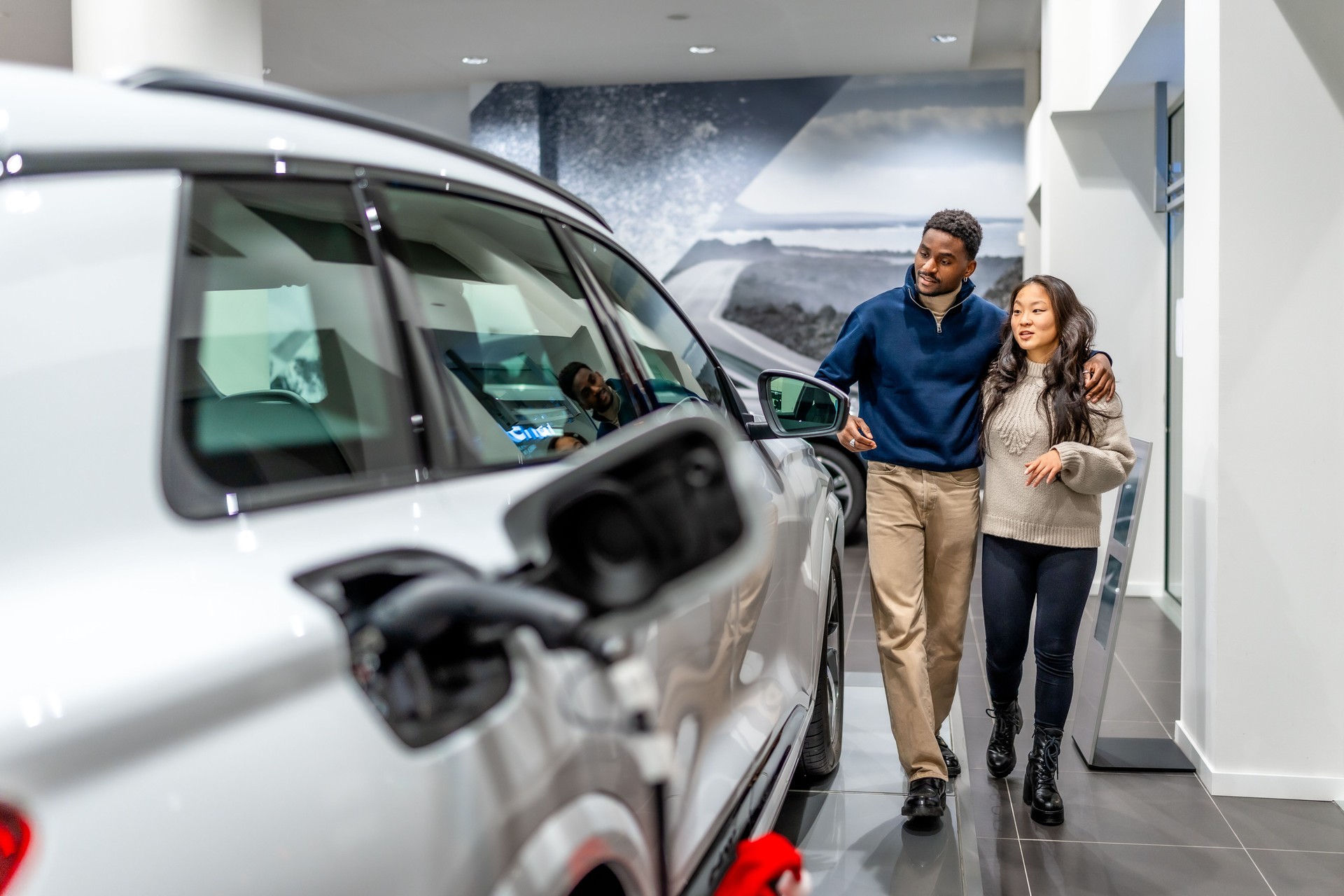 Happy multiethnic couple choosing electric car at dealership