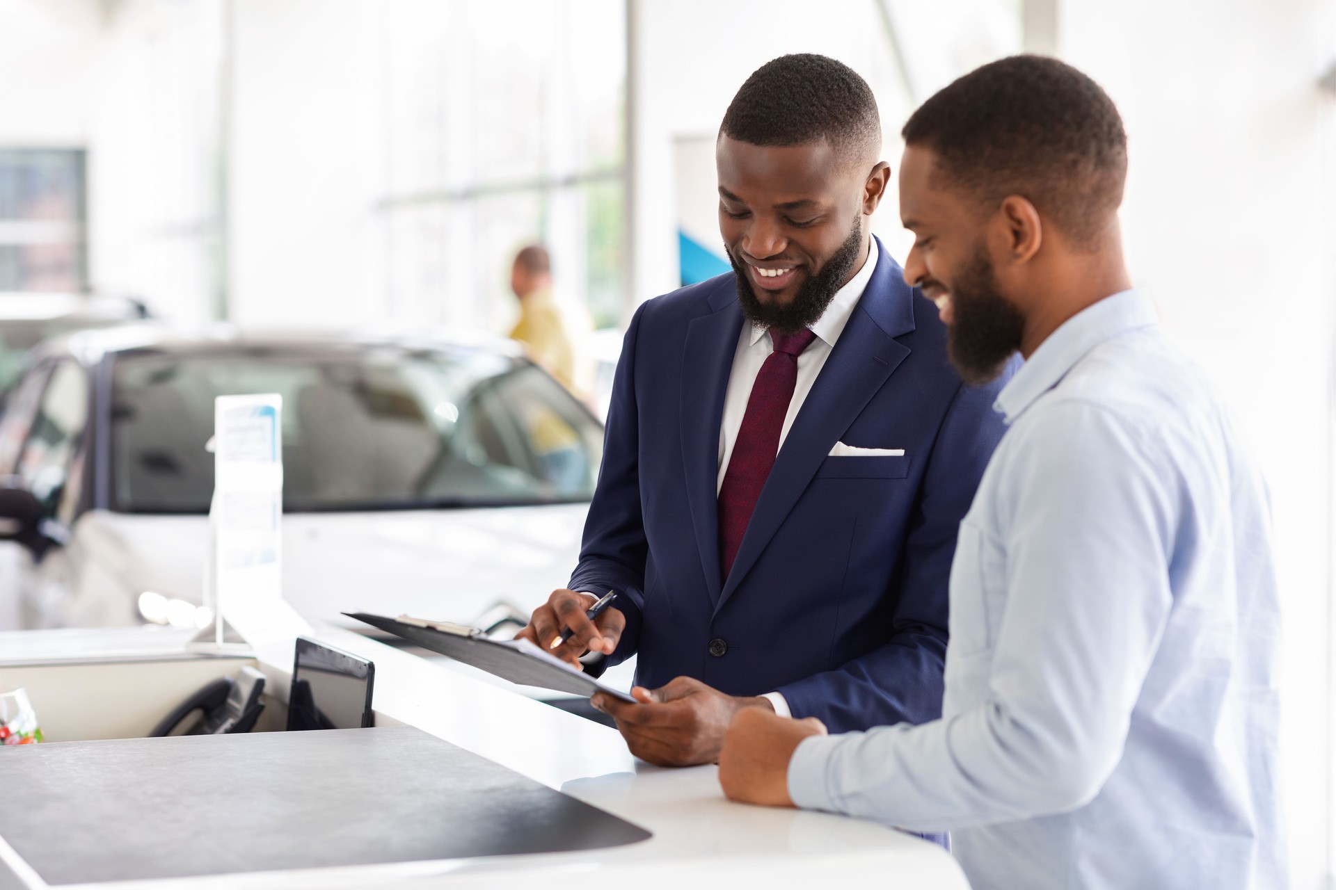 Joyful Black Man Buying Car, Signing Papers With Salesman In Dealership Office