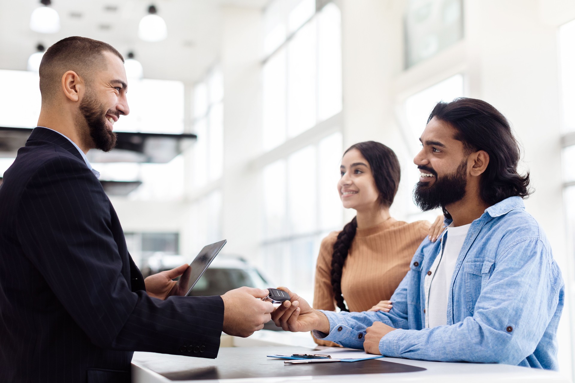 Smiling Couple Receives Car Keys From Salesman in Dealership Showroom